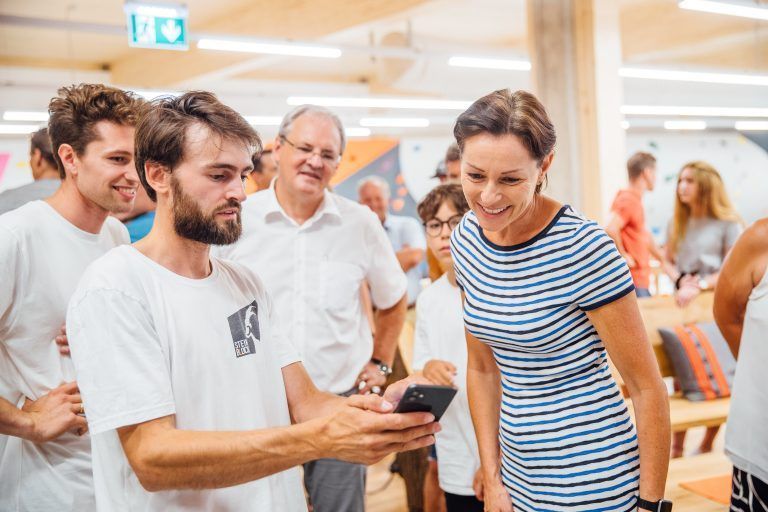 Landesrätin Martina Rüscher lässt sich die App für das Kilter Board zeigen. Das beobachtet Landtagspräsident Harald Sonderegger aus dem Hintergrund. <span class="copyright">sams</span>