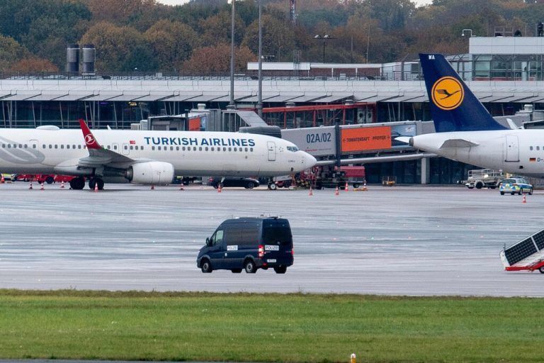 A police van observe the car of a hostage taker seen parked under a Turkish airline plane on the tarmac at the airport in Hamburg, northern Germany on November 5, 2023. Air traffic at Hamburg airport remained suspended Sunday over a suspected hostage situation on the tarmac involving a child, local authorities said.<br />A gunman rammed his car through the security area onto the apron where planes are parked on Saturday evening, firing two shots in the air and flinging two burning bottles out of the vehicle, police said. (Photo by NEWS5 / Schröder / NEWS5 / AFP)