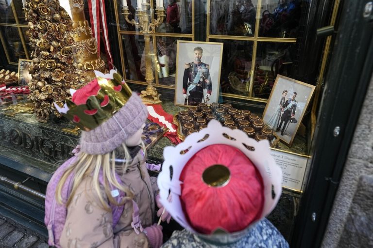 Children wearing crowns on their heads look at a picture of Crown Prince Frederik and his wife Crown Princess  Mary displayed in a window of a candy store in Copenhagen, Denmark, Sunday, Jan. 14, 2024. Denmark's Crown Prince Frederik takes over the crown on Sunday from his mother, Queen Margrethe II, who is breaking with centuries of Danish royal tradition and retiring after a 52-year reign. (AP Photo/Martin Meissner)