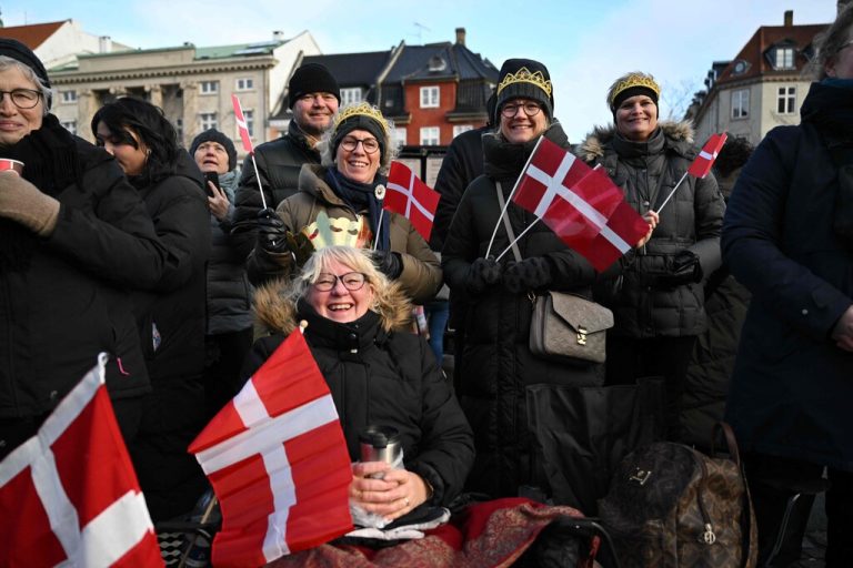 People wearing makeshit crowns and warm clothes wave flags of Denmark and react in the early in the morning at Christiansborg Palace Square ahead of the proclamation of abdication of Denmark's Queen Margrethe II, in Copenhagen, Denmark, on January 14, 2024. Denmark turns a page in its history on January 14 when Queen Margrethe abdicates and her son becomes King Frederik X, with more than 100,000 Danes expected to turn out for the unprecedented event. (Photo by Jonathan NACKSTRAND / AFP)