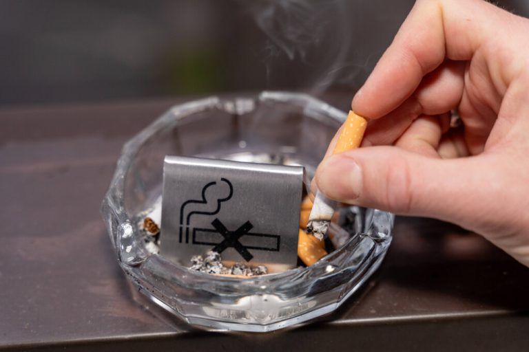 Bavaria, Germany - January 6, 2024: Smoke-free concept, a man puts out a burning cigarette in an ashtray with a no smoking sign *** Rauchfrei Konzept, ein Mann drückt eine brennende Zigarette in einem Aschenbecher mit einem Rauchverbot Schild aus