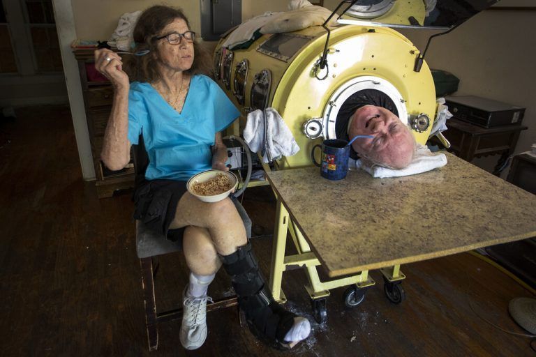 FILE - In this Friday, April 27, 2018 photo, attorney Paul Alexander chats with caregiver and friend Kathryn Gaines as he drinks coffee and she eats breakfast beside his iron lung at his home in Dallas. Alexander died Monday, March 11, 2024 at a Dallas hospital, said Daniel Spinks, a longtime friend. He said Alexander had recently been hospitalized after being diagnosed with COVID-19 but did not know the cause of death.  (Smiley N. Pool/The Dallas Morning News via AP)