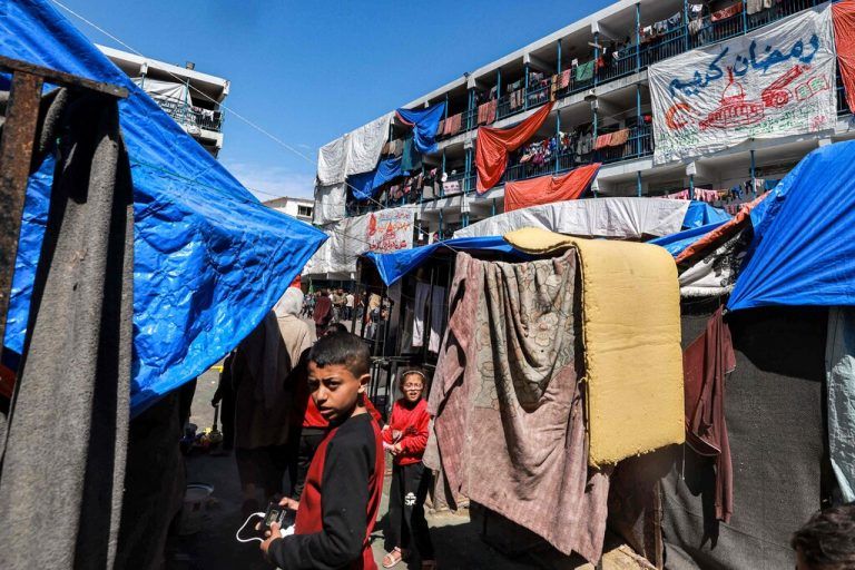 Sheets showing greeting messages for the Muslim holy month of Ramadan hang outside buildings at a camp sheltering displaced Palestinians erected in a school run by the United Nations Relief and Works Agency for Palestine Refugees (UNRWA) in Rafah in the southern Gaza Strip on March 13, 2024, amid the ongoing conflict between Israel and the militant group Hamas. (Photo by MOHAMMED ABED / AFP)