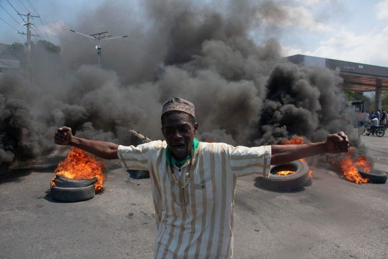 TOPSHOT - A protester reacts while tires burn in the street during a demonstration following the resignation of its Prime Minister Ariel Henry, in Port-au-Prince, Haiti, on March 12, 2024. A political transition deal in Haiti marks a key step forward for the violence-ravaged country but far more needs to be done, with some experts warning the situation could deteriorate further. (Photo by Clarens SIFFROY / AFP)