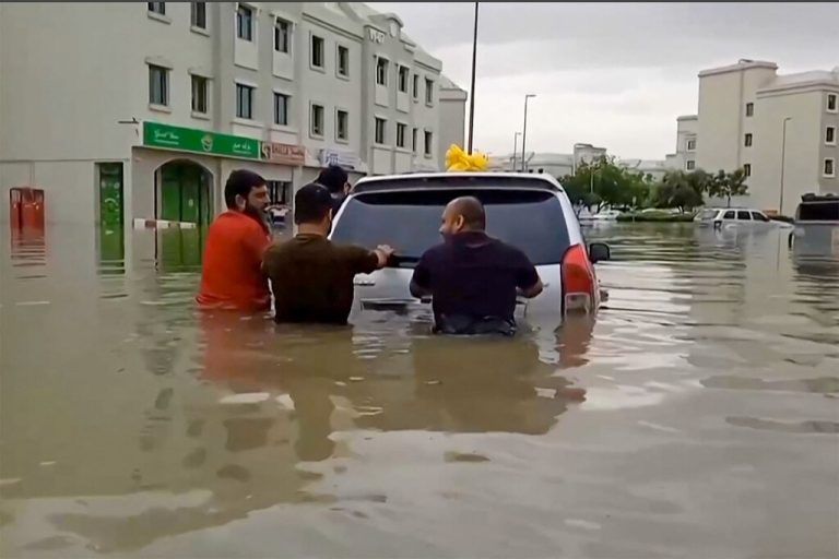 In this video grab from AFPTV, people push a stranded car along a flooded street in Dubai on April 16, 2024. Dubai, the Middle East's financial centre, has been paralysed by the torrential rain that caused floods across the UAE and Bahrain and left 18 dead in Oman on April 14 and 15. (Photo by ATIF BHATTI / ESN / AFP) / RESTRICTED TO EDITORIAL USE – MANDATORY CREDIT - AFP PHOTO / ATIF BHATTI / ESN - NO MARKETING NO ADVERTISING CAMPAIGNS – DISTRIBUTED AS A SERVICE TO CLIENTS -NO ARCHIVE -