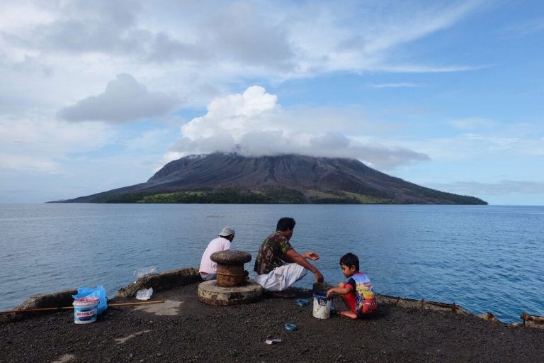 TOPSHOT - People fish at the port on Tagulandang island in Sitaro, North Sulawesi on April 19, 2024, as the Mount Ruang volcano is seen in the background spewing smoke. (Photo by Ronny Adolof BUOL / AFP)