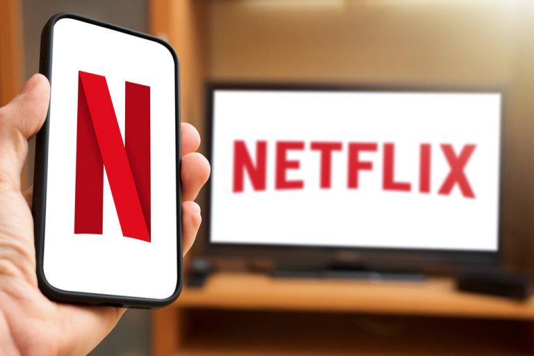 6 April 2024: Man holding smartphone with Netflix logo in front of a TV set with Netflix streaming provider logo. PHOTOMONTAGE *** Mann hält Smartphone mit Netflix Logo in der Hand vor einem TV Gerät mit Netflix Streaming Anbieter Logo. FOTOMONTAGE