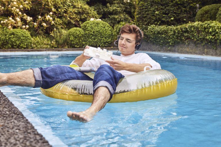 Young man working from home office on airbed in swimming pool looking at architectural model model released Symbolfoto property released UKOF00003