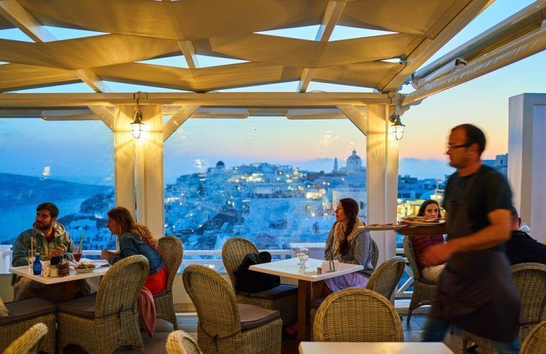 Tourists in luxury restaurants and on Oia Castle wait for the sunset with Caldera View and the famous Windmill in Oia, Santorini , Greece at 04 June 2019. Photographer: Peter Schatz