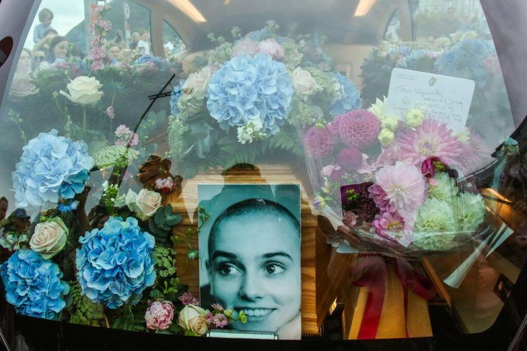 A photograph taken on August 8, 2023 shows the coffin and a picture of late Irish singer Sinead O'Connor, in the hearse during her funeral procession outside her former home in Bray, eastern Ireland, ahead of her funeral on August 8, 2023. A funeral service for Sinead O'Connor, the outspoken singer who rose to international fame in the 1990s, is to be held on Tuesday in the Irish seaside town of Bray. (Photo by PAUL FAITH / AFP)