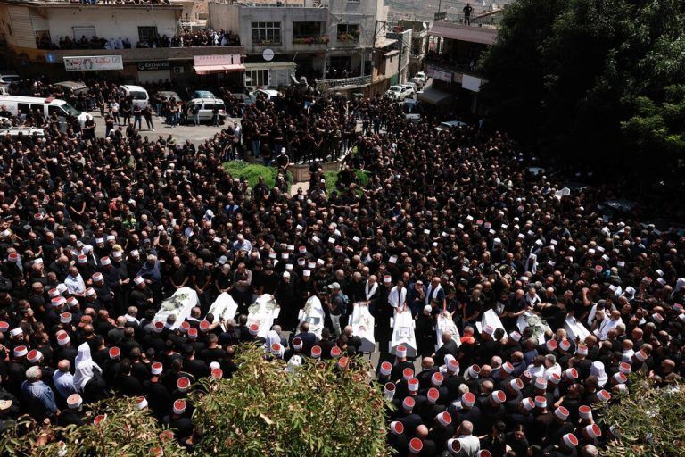 Druze elders and mourners surround the coffins of 10 of the 12 people killed in a rocket strike from Lebanon a day earlier, during a mass funeral in the Druze town of Majdal Shams in the Israel-annexed Golan Heights, on July 28, 2024. The Israeli military said the victims were struck by an Iranian-made rocket carrying a 50-kilogram warhead that was fired by Lebanese Hezbollah group at a soccer field in the Druze Arab town. Hezbollah has denied responsibility for the strike. (Photo by Menahem Kahana / AFP)