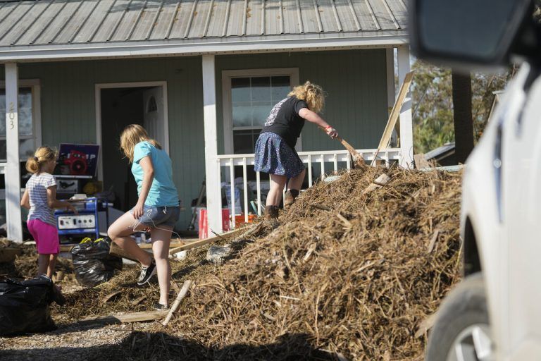 The Steen family picks rotten trash from the piles of seaweed that the storm surge carried to their home, in the aftermath of Hurricane Helene, in Steinhatchee, Fla., Saturday, Sept. 28, 2024. (AP Photo/Gerald Herbert)