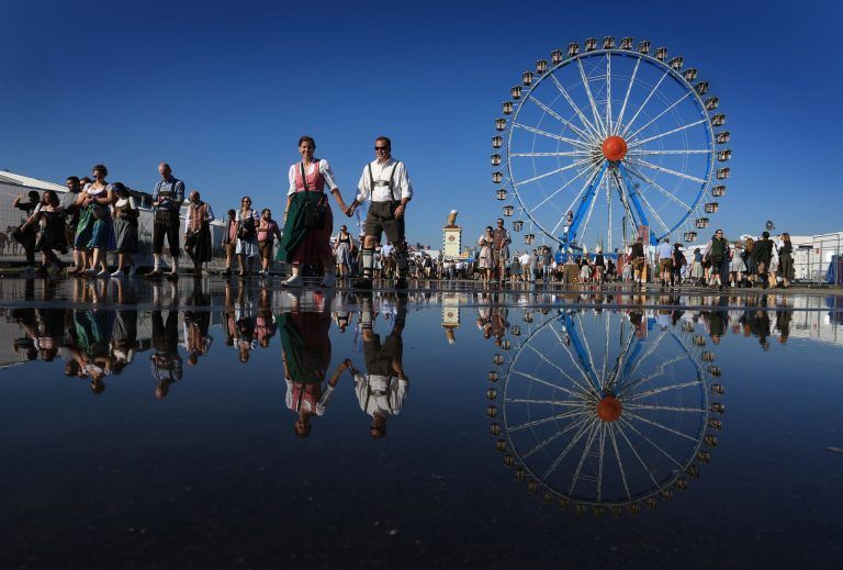 ABD0075_20240923 – MNCHEN – DEUTSCHLAND: 21.09.2024, Bayern, Mnchen: Oktoberfestbesucher und das Riesenrad spiegeln sich in einer Pftze. Die Wiesn findet vom 21. September bis 6. Oktober 2024 statt. Foto: Karl-Josef Hildenbrand/dpa +++ dpa-Bildfunk +++. – FOTO: APA/dpa/Karl-Josef Hildenbrand